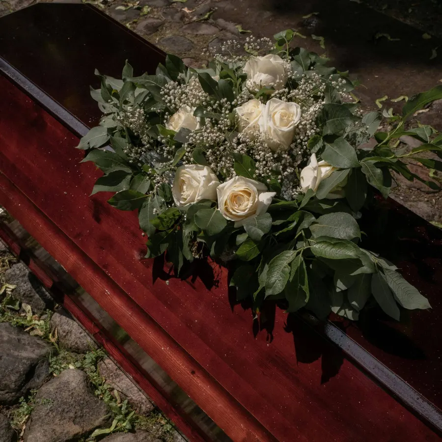 Brauner Sarg dekoriert mit Blumenstrauß aus weißen Rosen